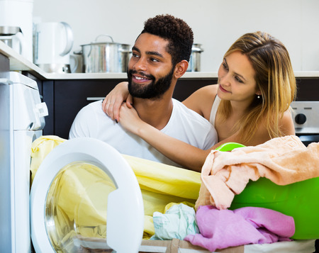 Afro husband helping white housewife to use washing machine in home interiorの写真素材