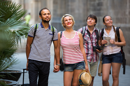 Two happy young smiling couples with travel bags walking through the cityの写真素材