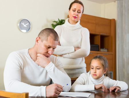Sad family with daughter reading financial documents at the table at homeの写真素材