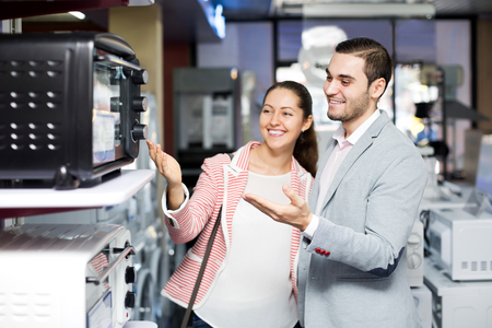 Cheerful family couple choosing new microwave in supermarket. Focus on the manの写真素材