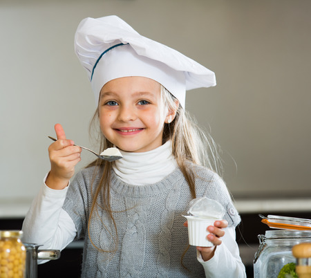 Little girl eating healthy yoghurt in kitchen and smilingの写真素材