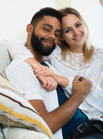 Happy spouses sitting on sofa, hugging and smiling indoorsの写真素材