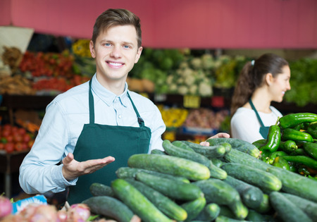 Two friendly young market stuff offering for retail slicing cucumbersの写真素材