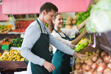 Friendly smiling sellers having vegetables and fruits on displays of market