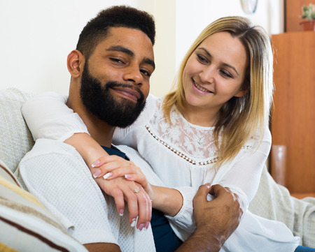 Happy spouses sitting on sofa, hugging and smiling indoorsの写真素材