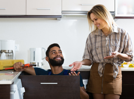 Young African plumber and smiling white housewife in domestic kitchenの写真素材