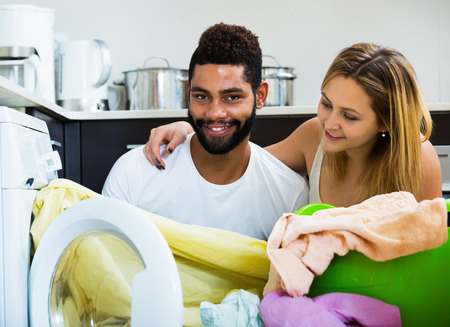 Afro husband helping white housewife to use washing machine at homeの写真素材