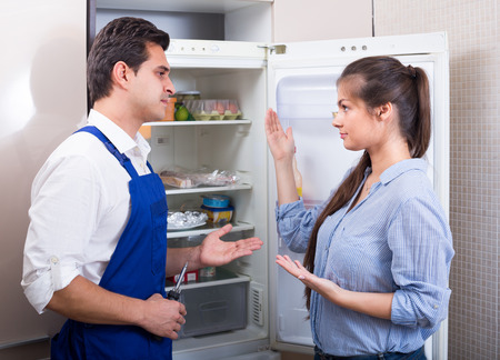 young woman complaining to handyman on problems with refrigeratorの写真素材
