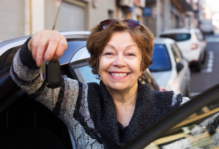 Happy senior woman posing near new car outdoors