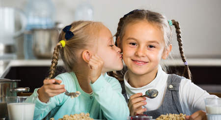 Portrait of smiling cute little sisters eating porridge in kitchenの写真素材