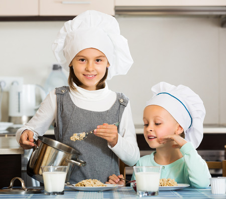 Two small girls eating healthy oatmeal at home kitchenの写真素材