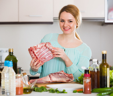 Cheerful young woman cooking mutton in home interiorの写真素材