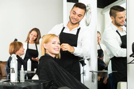 Hair stylist working on haircut for young beautiful woman. Focus on the womanの写真素材
