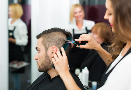 Professional woman hairdresser doing hairstyle for young menの写真素材