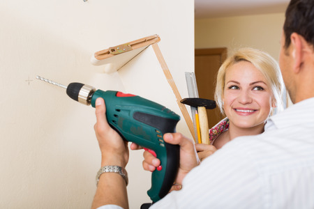 smiling couple hangs bookshelf on a wallの写真素材