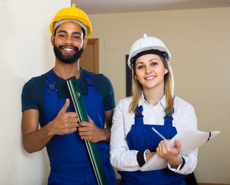 Portrait of smiling professional workers checking wall plane with level