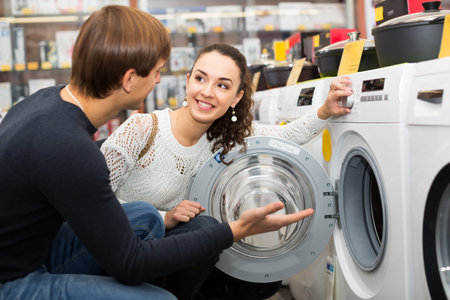 Happy young family couple buying new clothes washer in supermarketの写真素材