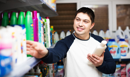 Smiling male customer choosing new shampoo in supermarket hair sectionの写真素材