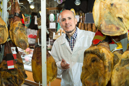 young seller with wurst and jamon in meat store counterの写真素材