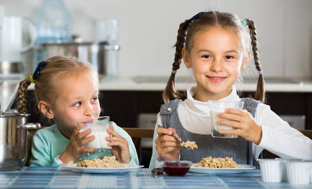 Portrait of happy smiling cute little sisters eating porridge in kitchenの写真素材