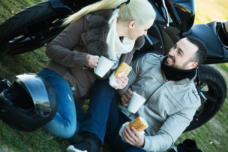 Young family couple posing near motor bike with sandwitches and coffee and smiling