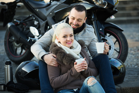 Portrait of couple drinking coffee and chatting near motorcycleの写真素材