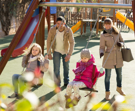 smiling american  family with two girls having fun on swings outdoors