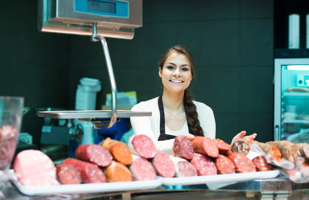 happy spanish female butcher with wurst and bologna in meat store counterの写真素材