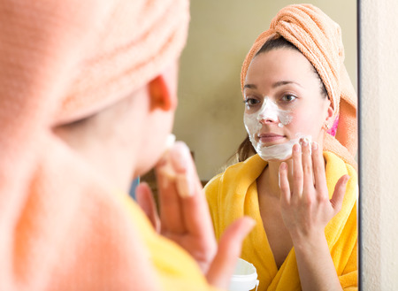 Reflection of a woman applying face scrub to her face in a mirror in a bathroomの写真素材