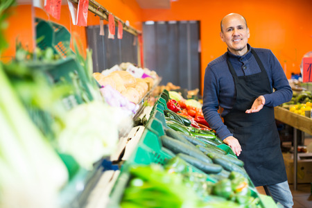 Portrait of friendly mature man in apron selling seasonal veggies at marketの写真素材