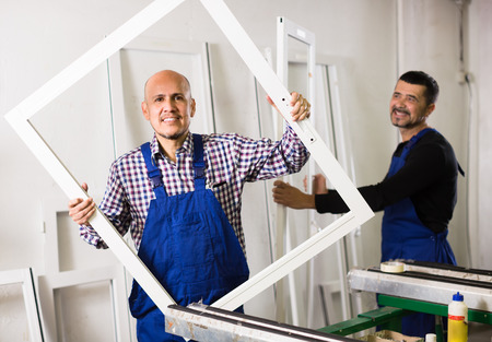 Two smiling workmen in coverall with different PVC windows and doorsの写真素材