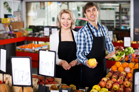 Portrait of positive mature woman and young man offering seasonal fruitsの写真素材