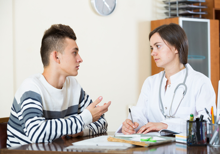 Male teenager and therapeutist at desk in modern clinicの写真素材