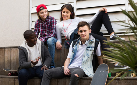 smiling european girl and three boys hanging out outdoors and discussing somethingの写真素材