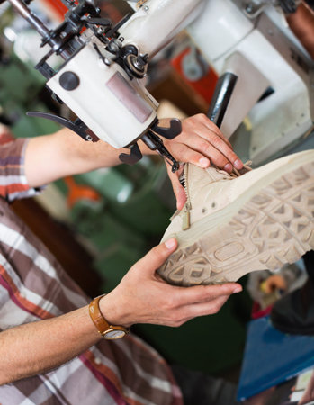 Mature diligent smiling workman sewing leather boots on stitch lathe in workshop