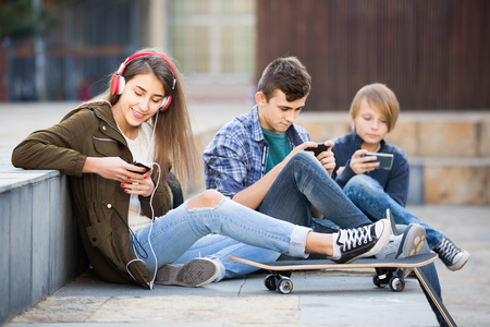 Three positive teenagers with smartphones in autumn day outdoorsの写真素材