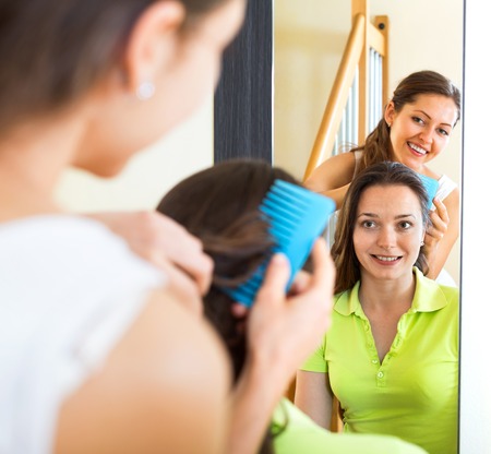 Young smiling girl doing hairstyle for her girlfriendの写真素材