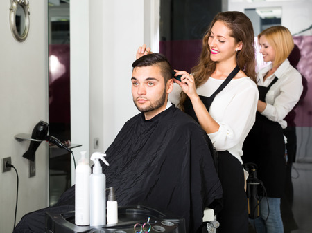 Group of people in a hairdressing salon. Hair stylists and their clients. Focus on manの写真素材