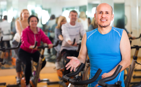 Group of adult people training in sport club on fitness cycle