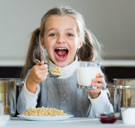Little girl eating tasty porridge at kitchen table indoorsの写真素材