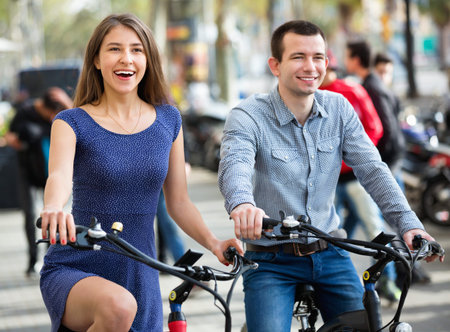 Cheerful  young man and woman with electrkc bikes in vacation on city street
