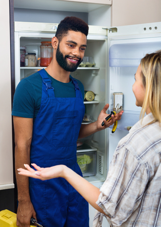 White young woman complaining to black handyman on problems with fridgeの写真素材