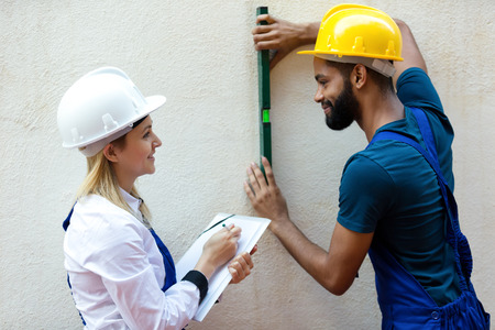 Smiling young technicians smoothing the wall surface at house. Focus on the womanの写真素材