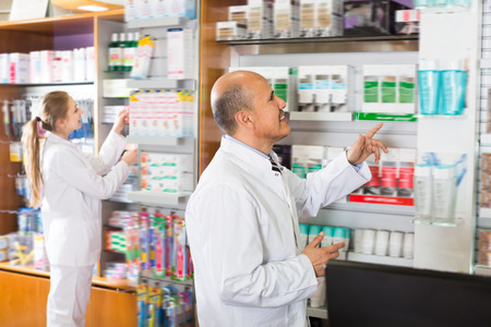 Adult pharmacist and pharmacy technician helping in drugstoreの写真素材
