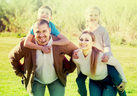 ?Portrait of young family of four people, mom and dad holding a girl and a boy up on the backの写真素材