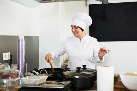 Positive mature woman cook wearing uniform standing on kitchenの写真素材