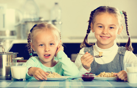 Two smiling cheerful girls eating healthy oatmeal at home kitchenの写真素材