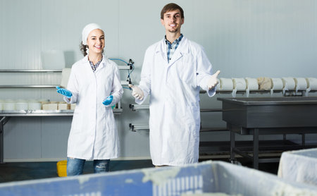 Portrait of young european man and woman dressed in lab coats are looking happy on the factory