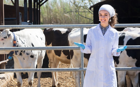 Young female veterinarian dressed in the white coat standing in the cowshed