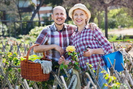 Smiling happy positive senior couple looking after flowers in the garden